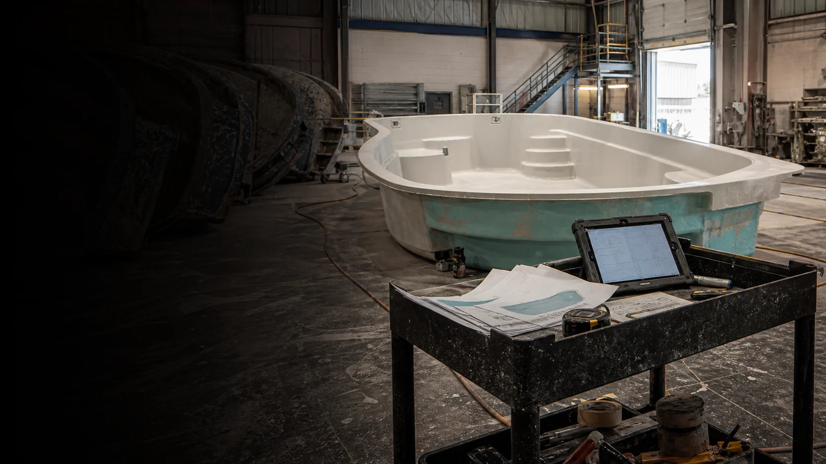 A fiberglass pool shell, configuration plans, and production tools on the factory floor.